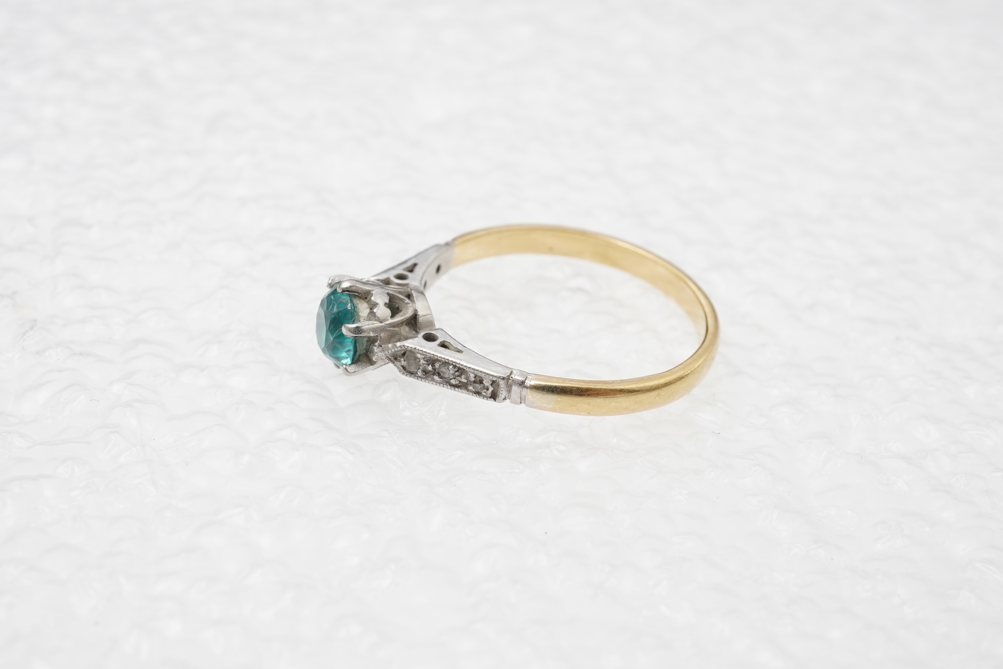A zircon and diamond ring, mid 20th century, claw-set with a brilliant-cut blue zircon measuring approximately 5mm diameter, to shoulders set with rose-cut diamonds, mounted in gold, size N, stamped 18CT, gross weight ap